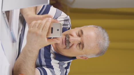 Vertical-video-of-Home-office-worker-old-man-talking-on-the-phone-facetime-happily.